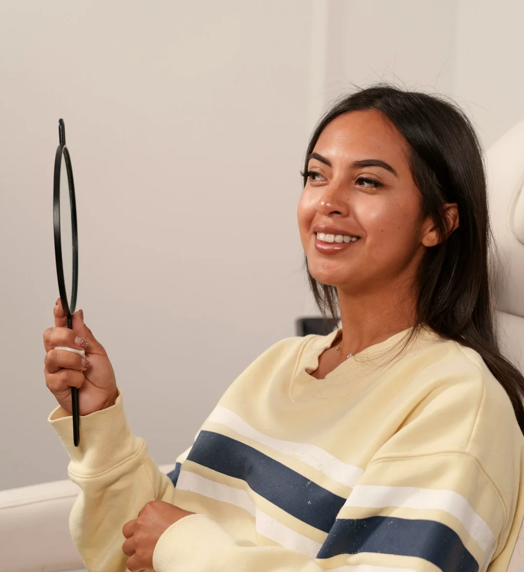 Patient sitting in a dental chair holding a hand mirror and smiling