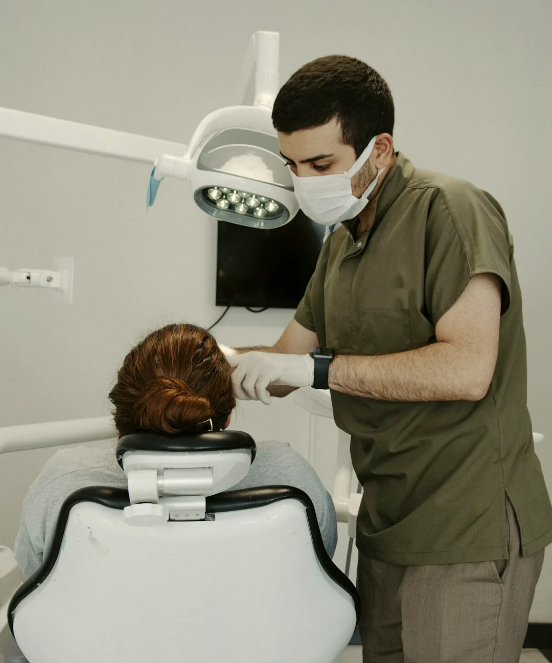 Dentist in olive scrubs performing a dental checkup for a patient